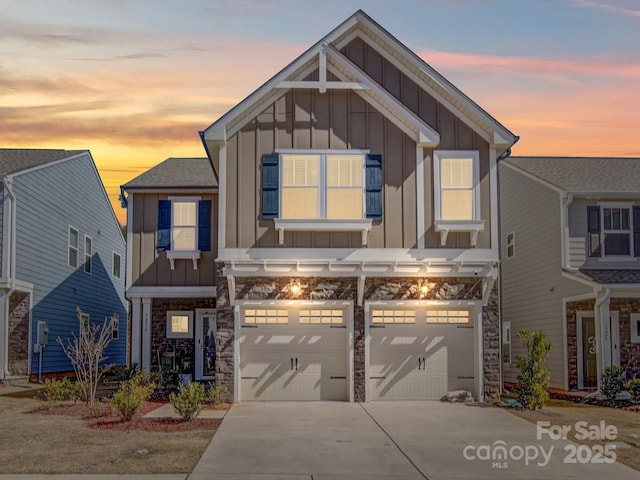 view of front of home with stone siding, board and batten siding, an attached garage, and driveway