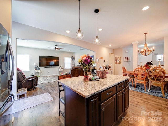 kitchen with light wood-style flooring, arched walkways, a kitchen breakfast bar, and freestanding refrigerator