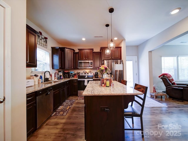 kitchen with dark wood-style flooring, a sink, a kitchen breakfast bar, appliances with stainless steel finishes, and a center island