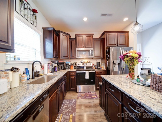 kitchen featuring visible vents, hanging light fixtures, stainless steel appliances, light wood-style floors, and a sink