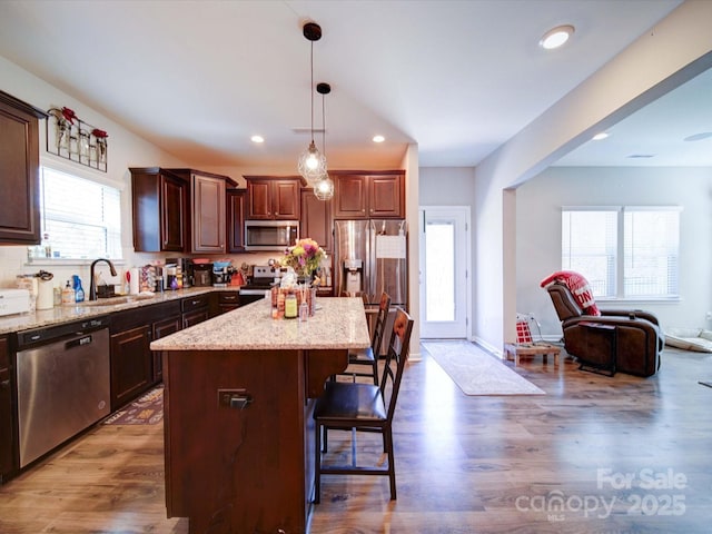 kitchen featuring light stone counters, appliances with stainless steel finishes, open floor plan, wood finished floors, and a kitchen breakfast bar