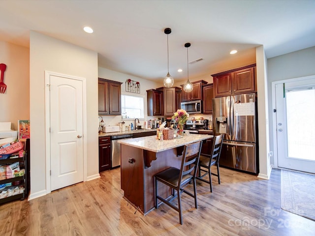 kitchen featuring appliances with stainless steel finishes, a breakfast bar area, light wood-style flooring, and visible vents