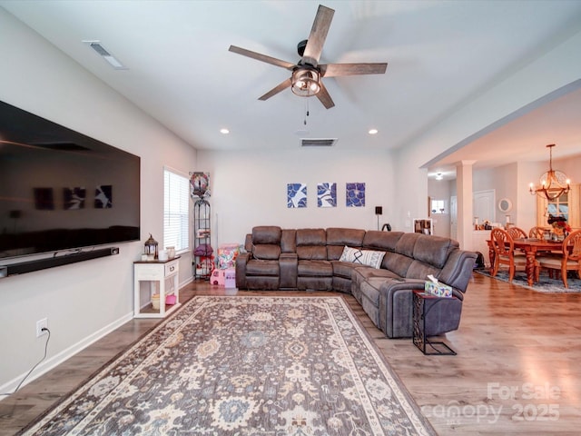 living area featuring ceiling fan with notable chandelier, wood finished floors, visible vents, and ornate columns