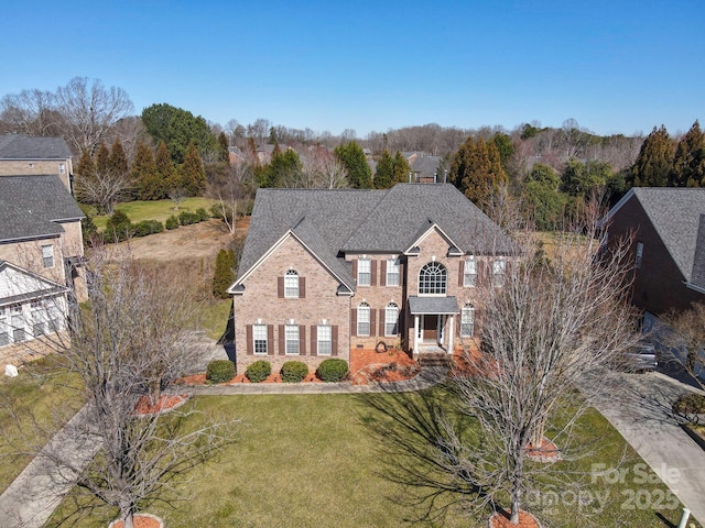 view of front of property featuring a front yard, brick siding, and roof with shingles