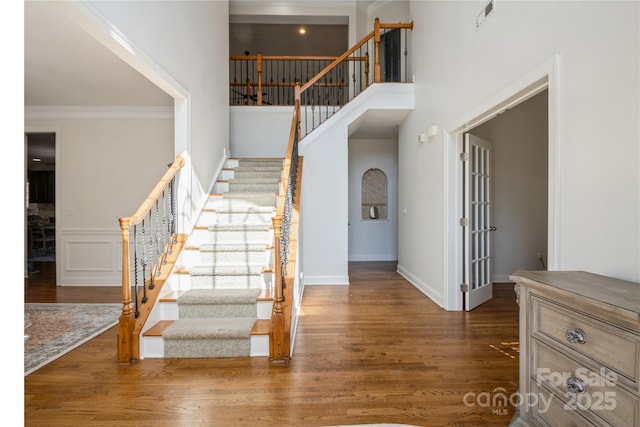 interior space with wood finished floors, a towering ceiling, visible vents, baseboards, and ornamental molding