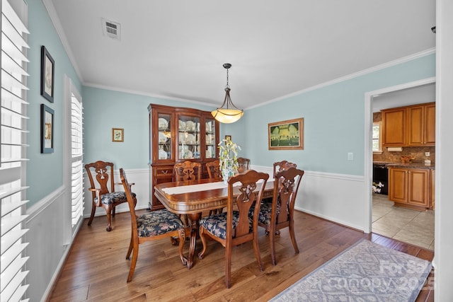 dining area with ornamental molding, light wood-type flooring, visible vents, and baseboards