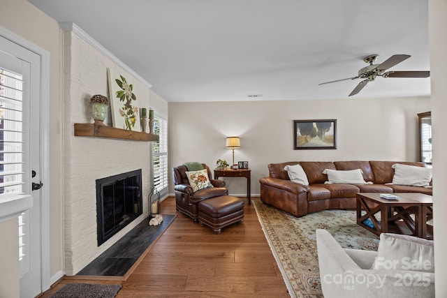 living room with ceiling fan, visible vents, a fireplace, and wood finished floors