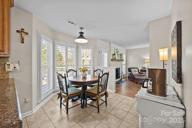 dining space with light tile patterned floors, a glass covered fireplace, visible vents, and baseboards