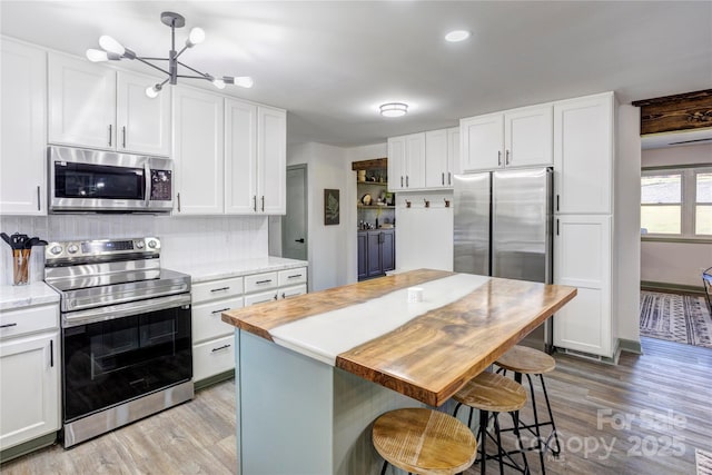 kitchen with stainless steel appliances, backsplash, white cabinetry, and light wood-style floors