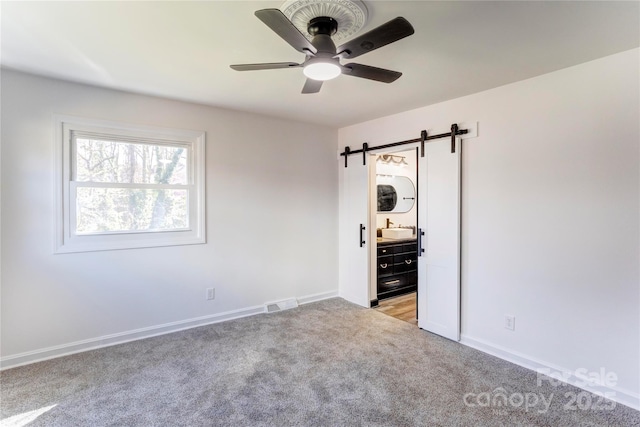 unfurnished room featuring ceiling fan, a barn door, light carpet, a sink, and visible vents