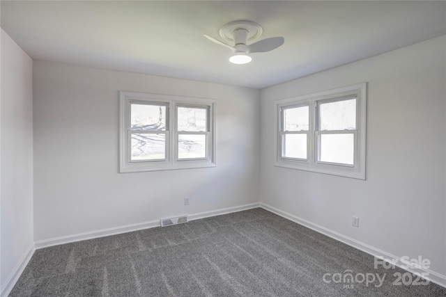 spare room with ceiling fan, dark carpet, visible vents, and baseboards