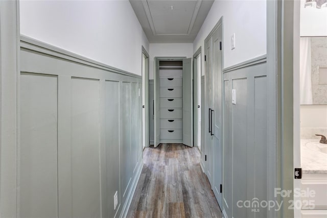 hall featuring attic access, a decorative wall, wood finished floors, and wainscoting