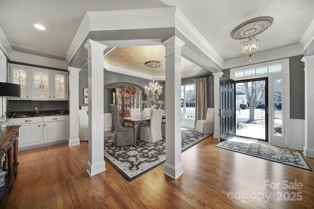 entrance foyer with an inviting chandelier, decorative columns, dark wood-style floors, and crown molding