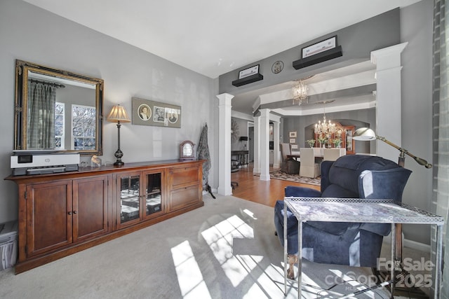 living area featuring light carpet, decorative columns, and a notable chandelier