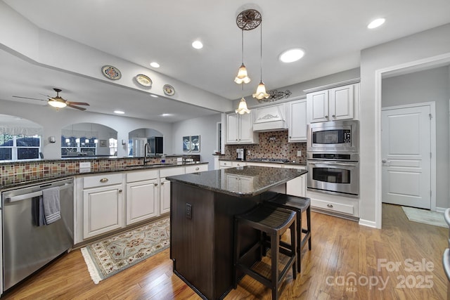 kitchen with light wood finished floors, decorative backsplash, appliances with stainless steel finishes, a breakfast bar, and a sink