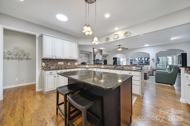 kitchen featuring arched walkways, a breakfast bar, open floor plan, a peninsula, and a sink