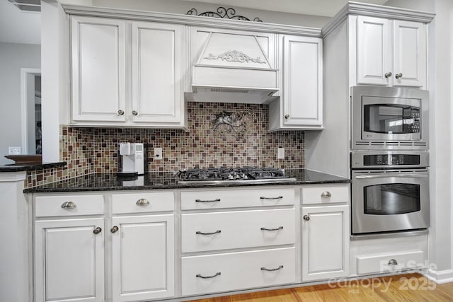 kitchen featuring appliances with stainless steel finishes, dark stone countertops, white cabinetry, and decorative backsplash