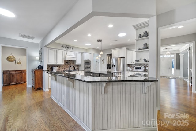 kitchen with visible vents, custom range hood, wood finished floors, stainless steel appliances, and open shelves