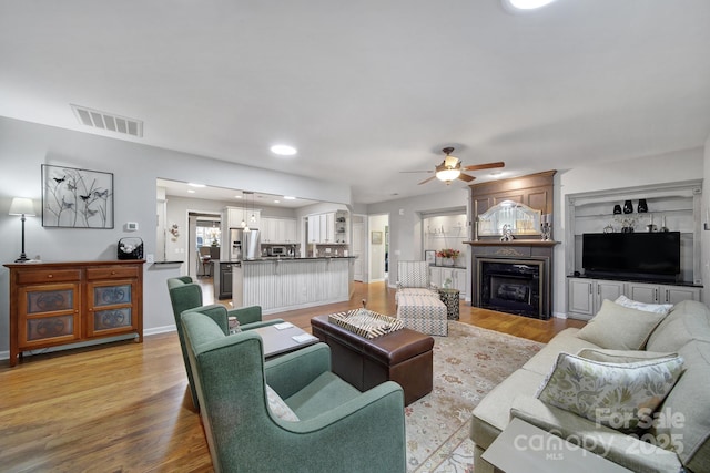 living area with visible vents, a fireplace, light wood finished floors, and ceiling fan