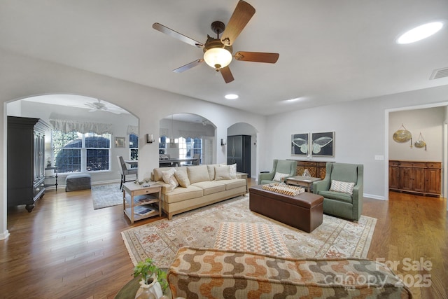 living room featuring arched walkways, wood finished floors, a ceiling fan, visible vents, and baseboards