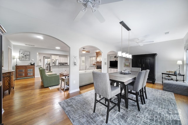 dining area with arched walkways, wood-type flooring, visible vents, baseboards, and ceiling fan with notable chandelier