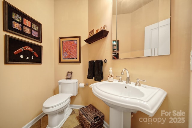 half bathroom featuring a sink, tile patterned flooring, toilet, and baseboards