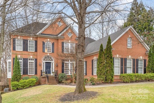 view of front of property featuring roof with shingles, a front lawn, and brick siding