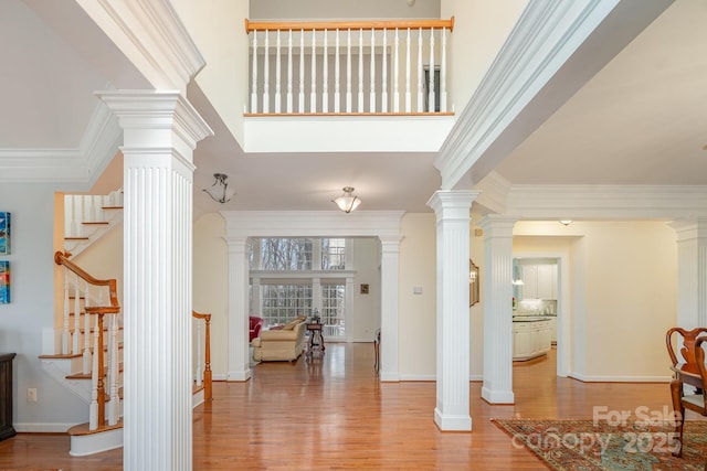 foyer entrance with ornamental molding, stairway, ornate columns, and wood finished floors