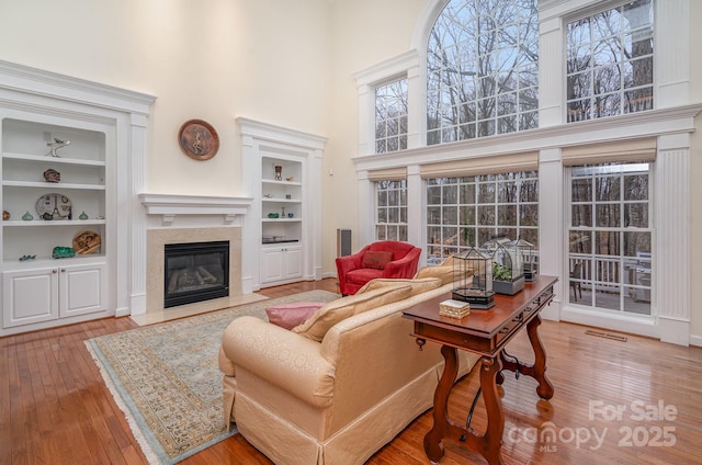 living area featuring built in features, wood-type flooring, visible vents, a high ceiling, and a high end fireplace