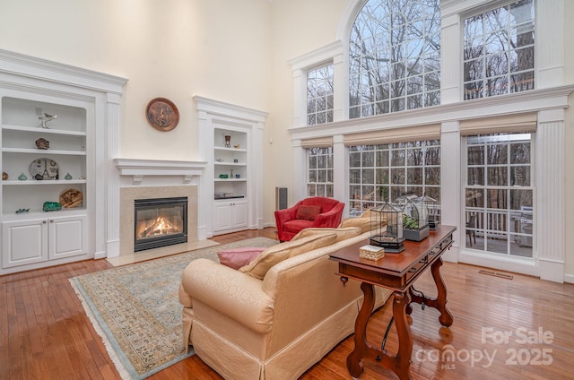 living room with built in shelves, a high ceiling, a fireplace, visible vents, and wood-type flooring