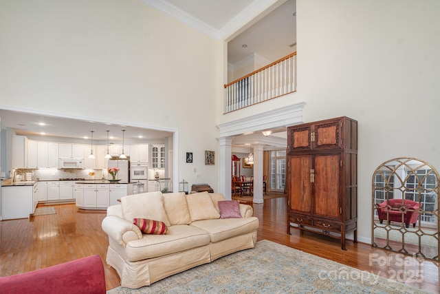 living area featuring a towering ceiling, ornate columns, light wood finished floors, and crown molding