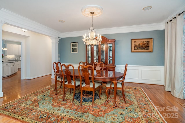 dining space with ornamental molding, light wood-style flooring, and ornate columns