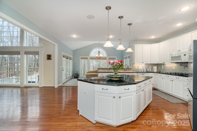 kitchen with pendant lighting, dark countertops, white microwave, white cabinets, and a sink