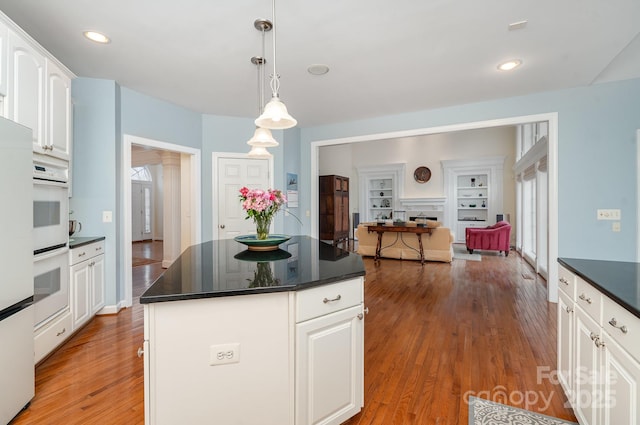 kitchen with dark countertops, open floor plan, a center island, hanging light fixtures, and white cabinetry