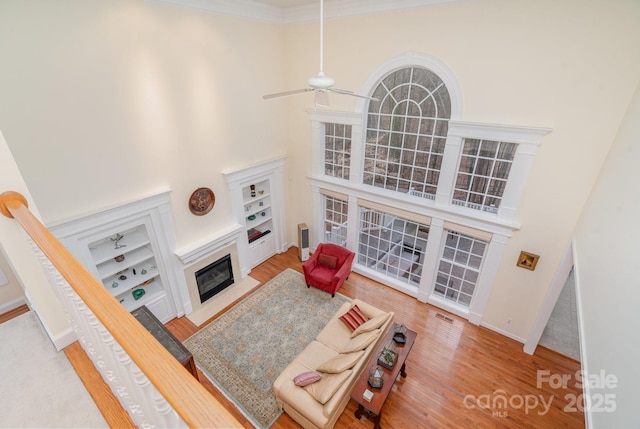 living room with a fireplace with flush hearth, a ceiling fan, a high ceiling, and wood finished floors