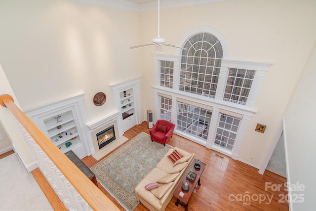 living room featuring built in shelves, a glass covered fireplace, a high ceiling, and wood finished floors