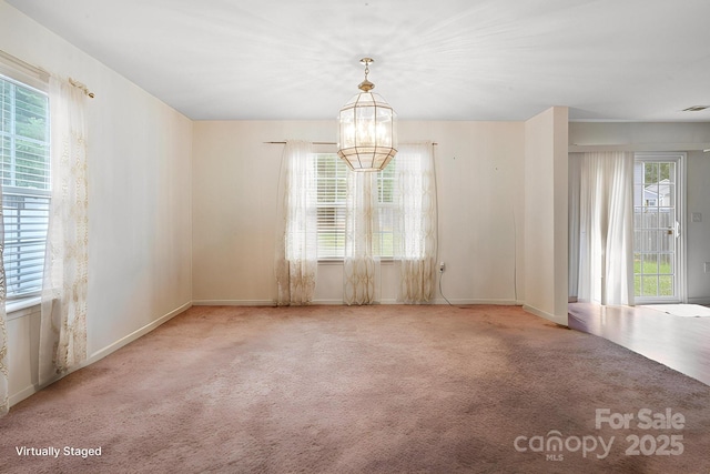 carpeted empty room featuring baseboards and a chandelier