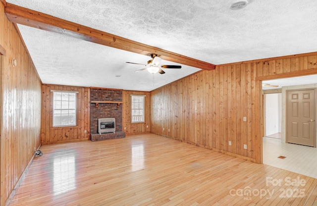 unfurnished living room with wood-type flooring, vaulted ceiling with beams, a textured ceiling, wood walls, and a fireplace