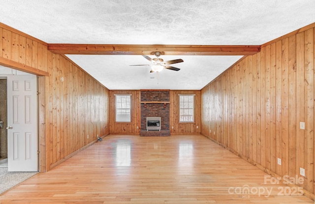 unfurnished living room with light wood-style flooring, a ceiling fan, a brick fireplace, wooden walls, and a textured ceiling