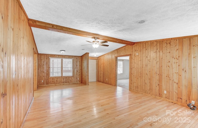 unfurnished room featuring light wood-type flooring, wood walls, plenty of natural light, and a textured ceiling