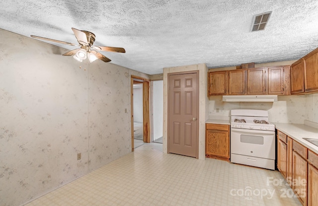 kitchen with brown cabinets, light floors, light countertops, white range with gas cooktop, and under cabinet range hood