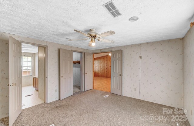 unfurnished bedroom featuring a textured ceiling, ceiling fan, ensuite bathroom, carpet flooring, and visible vents