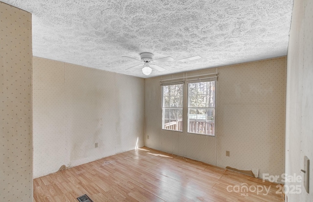 empty room featuring visible vents, ceiling fan, a textured ceiling, wood finished floors, and wallpapered walls