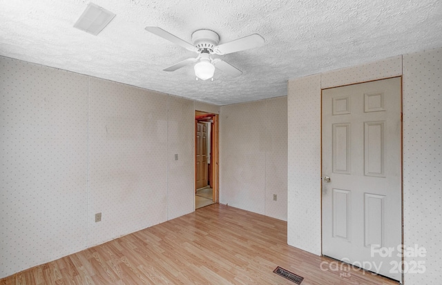 spare room featuring light wood-type flooring, wallpapered walls, visible vents, and a textured ceiling