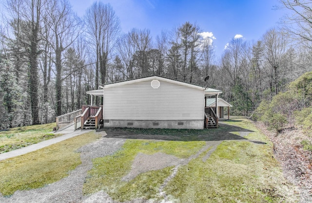 view of side of home featuring driveway, a yard, crawl space, and a wooded view