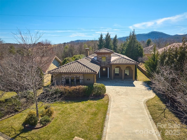 mediterranean / spanish-style home with driveway, stone siding, a tile roof, a front lawn, and stucco siding