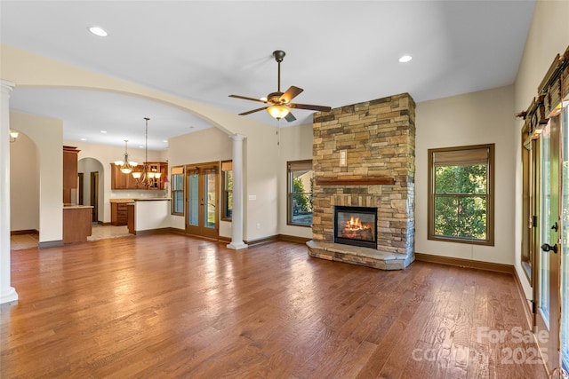 unfurnished living room with decorative columns, baseboards, wood finished floors, a fireplace, and ceiling fan with notable chandelier