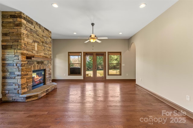 unfurnished living room featuring recessed lighting, arched walkways, wood finished floors, and a stone fireplace