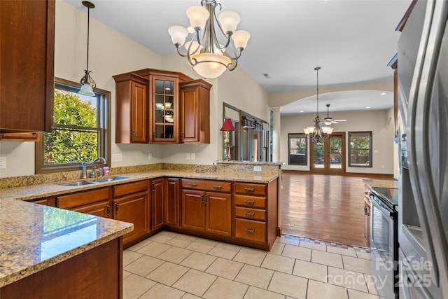 kitchen featuring appliances with stainless steel finishes, brown cabinets, a peninsula, an inviting chandelier, and a sink