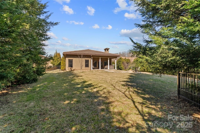 back of house featuring a tile roof, fence, a lawn, stucco siding, and a chimney